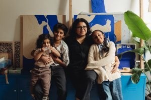 an image of Laxmi Hussain and her three children surrounding her shot in her art studio with pieces of her art behind them