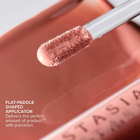 Image 2 - A close-up shot shows a fuzzy, flat-paddle shaped applicator covered in a peach-toned liquid lip product, emerging from its container, with text that reads FLAT-PADDLE SHAPED APPLICATOR Delivers the perfect amount of product with precision. Image 4 - The image shows a chart of makeup shades divided into two categories: Tinted Finish, described as Full-coverage, matte color with no shimmer, which includes shades Latte, Soft Pink, Deep Taupe, Sun Baked, Peachy Nude, Cotton Candy, Guava, Butterscotch, Caramel, Tan Rose, and Dusty Rose; and Shimmer Finish, described as Full-coverage color with dazzling sparkle & metallic sheen, which includes shades Honey Diamond, Amber Sparkle, Peachy, Goldy, Toffee Rose, Coral, Pink Ginger, Honey Kiss, and Cantaloupe. Image 5 - Two Anastasia Beverly Hills lip gloss tubes, one closed and one open with the wand exposed, lie on a white surface with swatches of the pink and shimmery bronze gloss, alongside text describing product features: ANASTASIA BEVERLY HILLS, HIGHLY-PIGMENTED, ULTRA-SMOOTH FORMULA WITH SEAMLESS GLIDE-ON, HIGH-SHINE, NON-STICKY FINISH WITH COMFORTABLE WEAR, LIGHT-REFLECTING SHADES IN TINTED + SHIMMER FINISHES. Image 6 - A close-up shows glossy lips with shimmery pink lip gloss being applied by a flat-paddle applicator, accompanied by the text: HOW TO APPLY Apply to the center of the top and bottom lip. Use the tip of the flat-paddle applicator to shape the lip line with precision. Image 7 - A close-up shows a persons glossy pink lips with a lip gloss applicator applying more product to the lower lip, with the text Pair with Lip Liner for a defined + sculpted look. Image 8 - A close-up of a woman with long dark hair and makeup, including pink blush and glossy pink lips, wearing a two-tone ear cuff and a gold ring with pink stones on her right hand. MODEL WEARS | COTTON CANDY