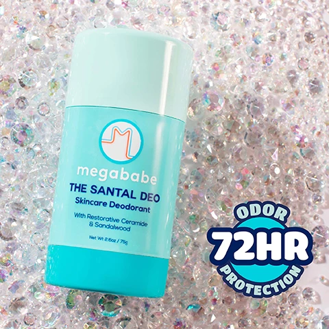 Image 1 - A light blue Megababe deodorant stick with a pale green top is shown against a glittering background of clear crystals, displaying the text megababe, THE SANTAL DEO, Skincare Deodorant, With Restorative Ceramide & Sandalwood, Net Wt 2.6oz / 75g, and a graphic in the bottom right corner states ODOR 72HR PROTECTION. Image 2 - A light blue and turquoise Megababe The Santal Deo Skincare Deodorant stick is positioned on a pink surface next to a piece of driftwood and a white flower petal, with text on the product reading megababe, THE SANTAL DEO, Skincare Deodorant, With Restorative Ceramide & Sandalwood, Net Wt 2.6oz / 75g, and additional text at the bottom stating Classic santal scent with hints of violet & amber. Image 3 - A teal Megababe THE SANTAL DEO Skincare Deodorant stick, open to show the white product, sits on a pink and teal background next to a smear of the product, with additional text reading Calming sandalwood soothes skin, Restorative ceramides support a healthy skin barrier, With Restorative Ceramide & Sandalwood, and Net Wt. 2.65 oz / 75g. Image 4 - A teal blue Megababe deodorant stick with its cap off is shown on a reflective surface against a purple background, with a yellow sun icon on the top left that reads Dont leave me in the sun I MIGHT MELT! and text on the product that says megababe THE SANTAL DEO Skincare Deodorant With Restorative Ceramide & Sandalwood Net Wt 2.6oz / 75g. Image 5 - A person holds a teal blue deodorant stick to their armpit, demonstrating how to use the product, with text on the image reading How to: The Santal Deo, STEP 1: Apply daily as often as needed to clean, dry skin, STEP 2: Allow 2 weeks for pits to adjust from a traditional antiperspirant, and the deodorant itself is labeled megababe THE SANTAL DEO 2.6 oz / 73g Deodorant. Image 6 - A hand holds a light blue and teal Megababe The Santal Deo skincare deodorant stick, with text to the left listing No aluminum, No baking soda, No parabens, No sulfates, No phthalates, and the product itself displaying megababe THE SANTAL DEO Skincare Deodorant With Restorative Ceramide & Sandalwood Net Wt 2.6oz / 75g. Image 7 - A guide on how to properly open deodorant, displayed on a pink background with a blue border, featuring an icon of twisting rings with arrows, with the text: Open your deo the right way! TWIST DONT PULL. Megababe deodorants are made with 100% natural ingredients, so theyre super gentle (just like your skin!). To keep your deo in perfect shape, follow these easy steps when opening: Pulling the inner dome straight off can cause your deo to break inside—oh no! Instead: Twist up the deodorant slightly until a little product peeks out. Gently twist off the inner dome to release pressure before use. Keep your deo happy & ready to swipe!