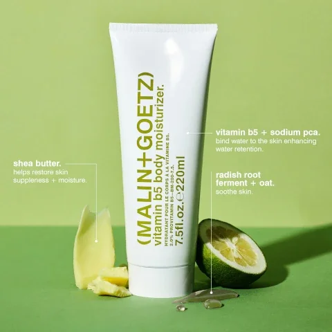 A white tube of Malin+Goetz Vitamin B5 body moisturizer stands upright on a green background, with chunks of shea butter on the left and a sliced lime and liquid droplets on the right, accompanied by text detailing ingredients and their benefits: MALIN+GOETZ vitamin b5 body moisturizer. HYDRATANT POUR LE CORPS À LA VITAMINE B5. 2.0% PROVITAMIN B5. 7.5fl.oz.e220ml. shea butter. helps restore skin suppleness + moisture. vitamin b5 + sodium pca. bind water to the skin enhancing water retention. radish root ferment + oat. soothe skin.